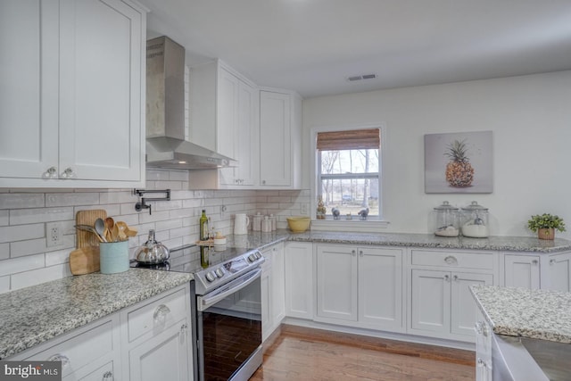 kitchen with white cabinetry, electric range, wall chimney range hood, and tasteful backsplash