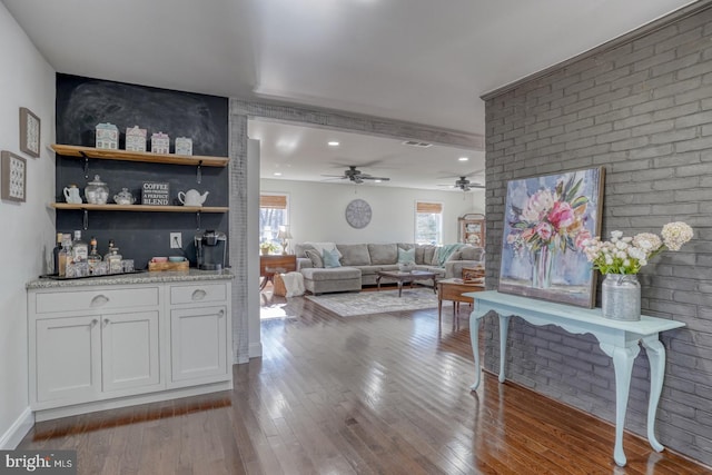 living area featuring dark wood finished floors, visible vents, and brick wall