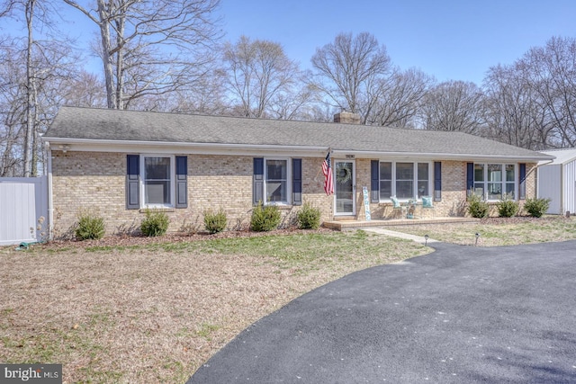 ranch-style home with brick siding, a chimney, fence, and a shingled roof