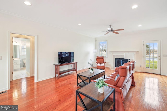 living room featuring baseboards, crown molding, light wood-style floors, a fireplace, and recessed lighting