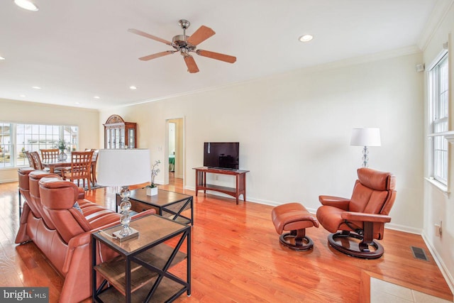 living room featuring baseboards, light wood-type flooring, visible vents, and crown molding