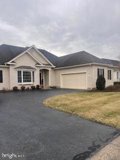 ranch-style home featuring aphalt driveway, an attached garage, and a front yard