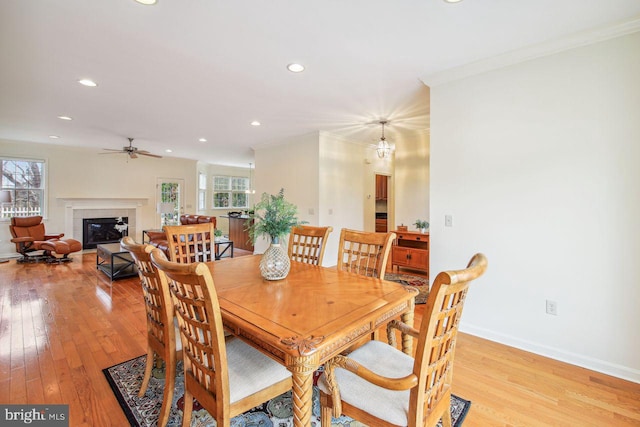 dining space with light wood-style floors, a glass covered fireplace, crown molding, and baseboards