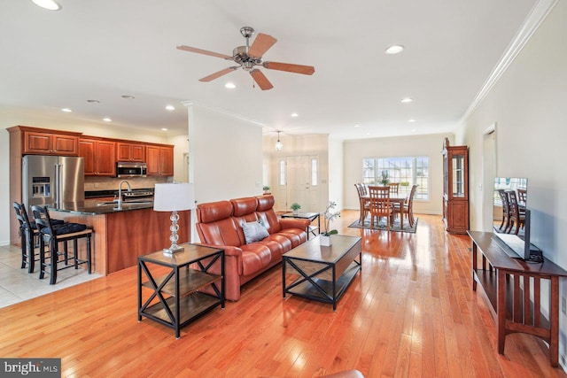 living area with light wood finished floors, baseboards, a ceiling fan, ornamental molding, and recessed lighting