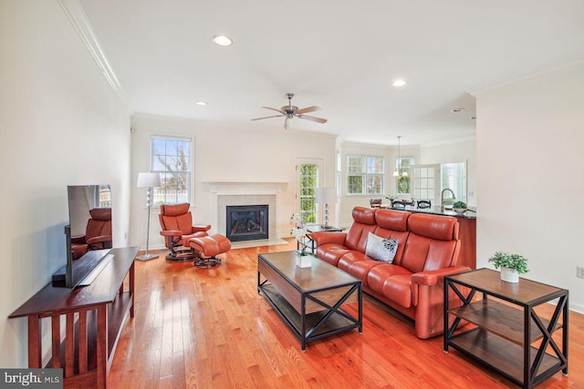 living room with ornamental molding, light wood finished floors, a tiled fireplace, and a healthy amount of sunlight