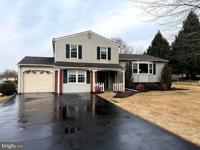 split level home with aphalt driveway, roof with shingles, an attached garage, a front yard, and brick siding