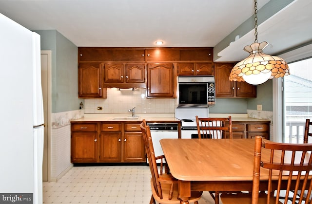 kitchen featuring dishwashing machine, stainless steel microwave, freestanding refrigerator, light floors, and a sink