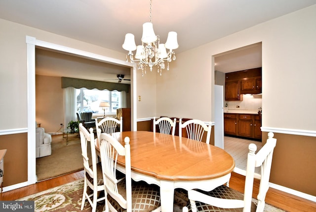 dining room featuring ceiling fan with notable chandelier, light wood finished floors, and baseboards