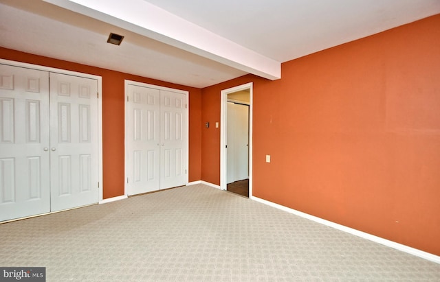 unfurnished bedroom with multiple closets, carpet, beamed ceiling, and baseboards