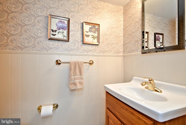 bathroom featuring a wainscoted wall, vanity, and wallpapered walls