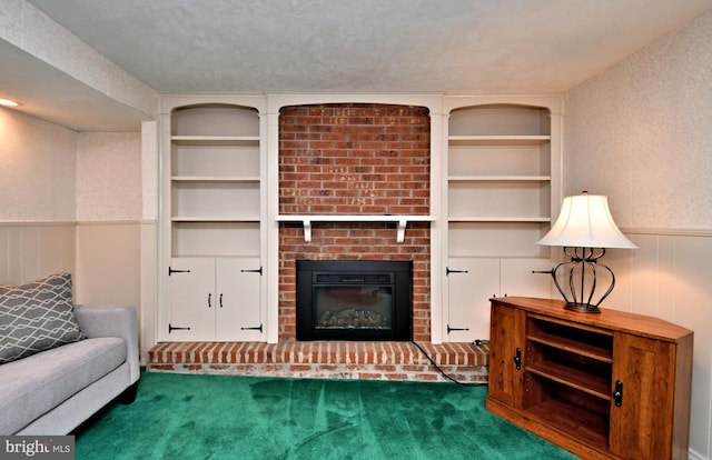 carpeted living room featuring a textured ceiling, built in shelves, wainscoting, and a brick fireplace