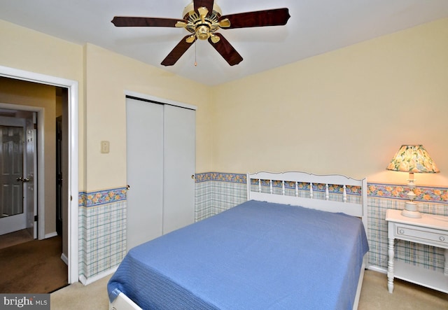 carpeted bedroom with a wainscoted wall, a ceiling fan, and a closet