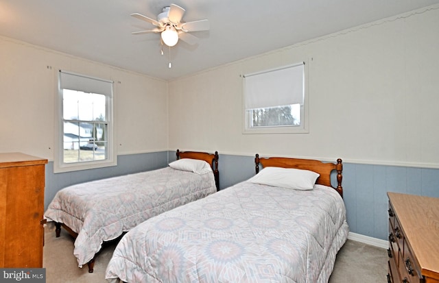 bedroom with light carpet, ceiling fan, and wainscoting