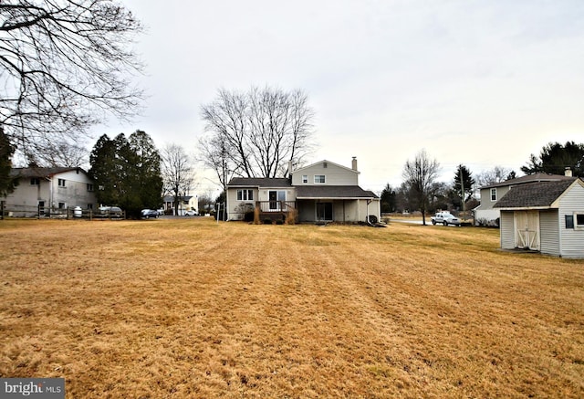 rear view of house featuring a yard, a chimney, a storage unit, and an outbuilding