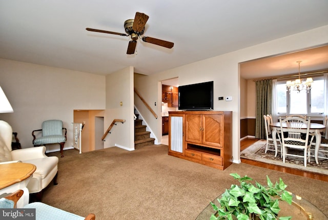 carpeted living area with stairs and ceiling fan with notable chandelier