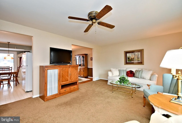 living room featuring ceiling fan, baseboards, and light colored carpet