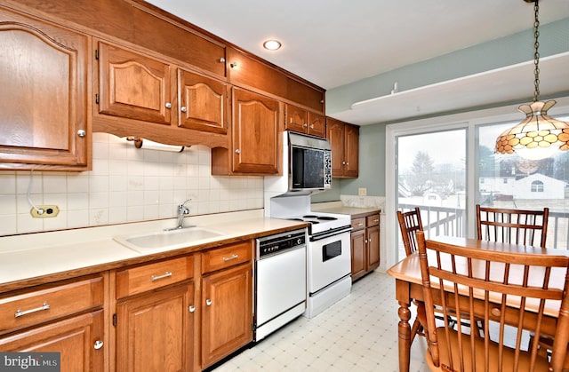 kitchen with light floors, light countertops, brown cabinetry, a sink, and white appliances