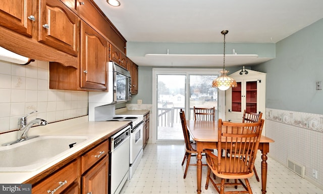 kitchen featuring light floors, brown cabinets, a sink, and a wainscoted wall