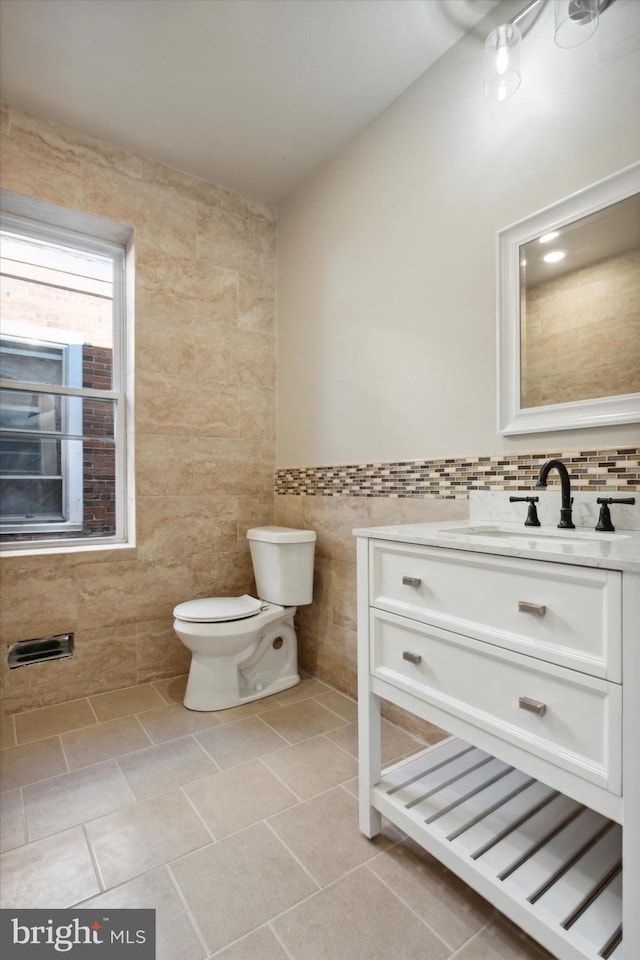 half bathroom featuring toilet, vanity, tile walls, and tile patterned floors