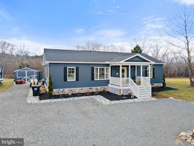 view of front of home with a porch, a shingled roof, an outdoor structure, driveway, and a front yard