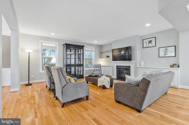 living area with recessed lighting, light wood-style floors, and a glass covered fireplace