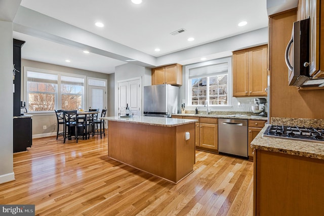 kitchen with light stone countertops, visible vents, light wood-style floors, appliances with stainless steel finishes, and a center island