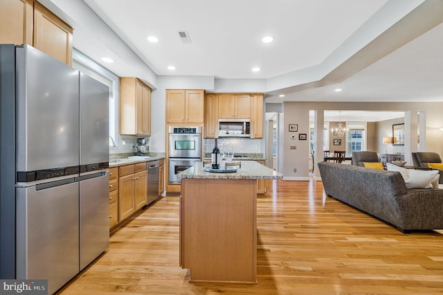 kitchen featuring visible vents, a center island, open floor plan, light wood-type flooring, and appliances with stainless steel finishes