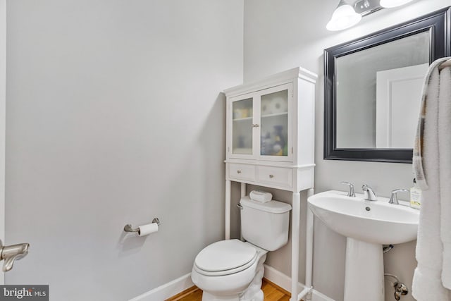 half bath with toilet, wood finished floors, baseboards, and a sink