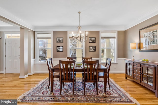 dining room featuring light wood-type flooring, baseboards, a notable chandelier, and crown molding