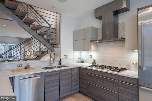 kitchen with a sink, light countertops, appliances with stainless steel finishes, wall chimney exhaust hood, and tasteful backsplash