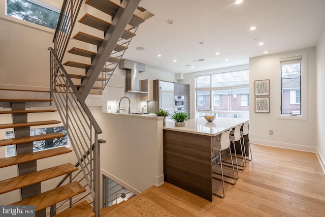 kitchen with wall chimney exhaust hood, light countertops, light wood-style flooring, and recessed lighting