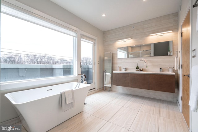 bathroom featuring double vanity, recessed lighting, a shower stall, a freestanding tub, and tile patterned floors