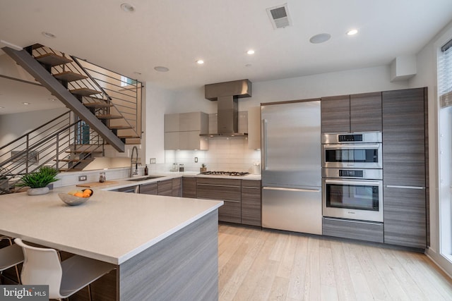 kitchen featuring light countertops, visible vents, appliances with stainless steel finishes, wall chimney range hood, and modern cabinets