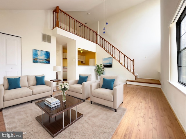 living area with visible vents, a towering ceiling, light wood-type flooring, baseboards, and stairs