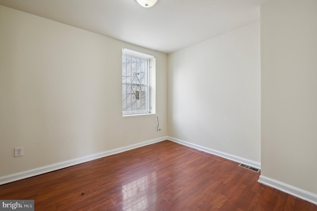 unfurnished room featuring dark wood-style floors, visible vents, and baseboards