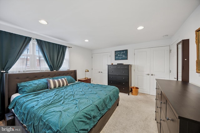 bedroom featuring light carpet, two closets, and recessed lighting