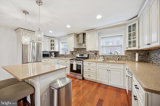 kitchen featuring light wood finished floors, a kitchen bar, appliances with stainless steel finishes, a sink, and wall chimney exhaust hood