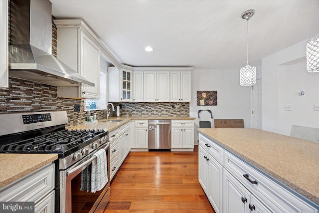 kitchen with a sink, appliances with stainless steel finishes, decorative backsplash, wall chimney exhaust hood, and light wood finished floors