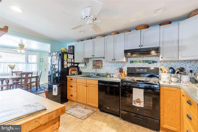 kitchen with under cabinet range hood, a sink, light countertops, black appliances, and tasteful backsplash