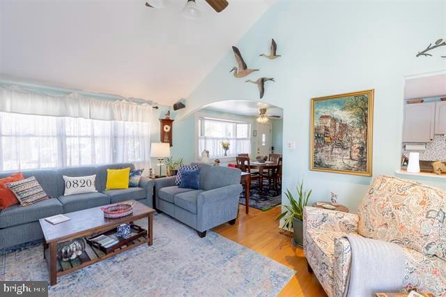 living area featuring arched walkways, high vaulted ceiling, wood finished floors, and a ceiling fan