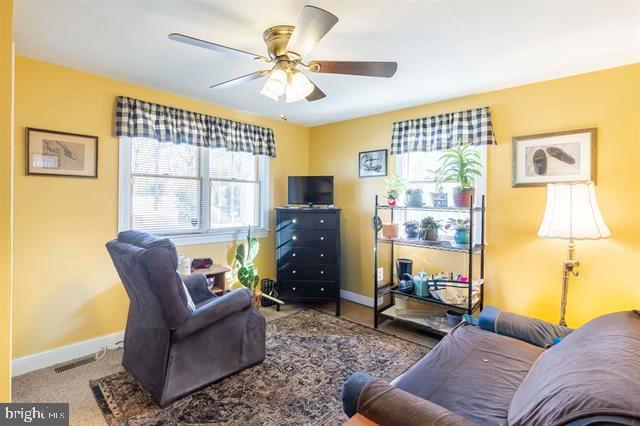 living area featuring baseboards, visible vents, a ceiling fan, and carpet flooring