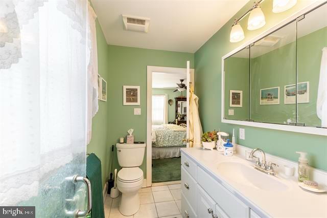 ensuite bathroom with visible vents, connected bathroom, toilet, tile patterned floors, and vanity