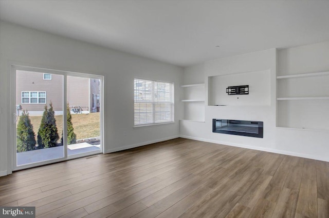 unfurnished living room featuring baseboards, wood finished floors, a glass covered fireplace, and built in features