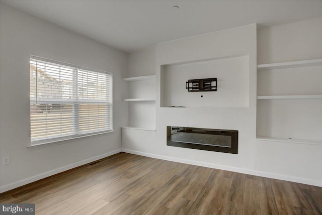 unfurnished living room with built in features, visible vents, a glass covered fireplace, wood finished floors, and baseboards