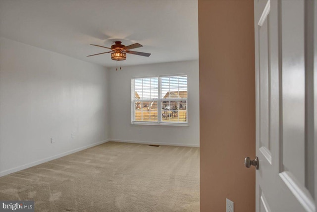 spare room with light carpet, ceiling fan, visible vents, and baseboards