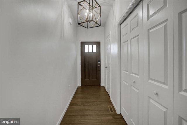 doorway to outside with dark wood-style floors, a notable chandelier, visible vents, and baseboards