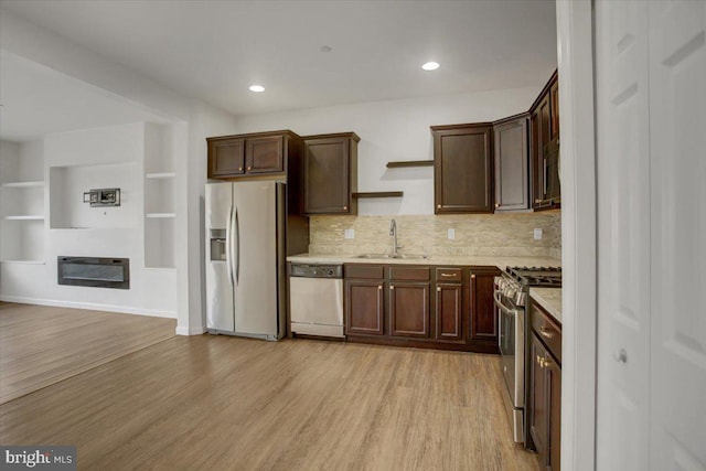 kitchen featuring light wood-style flooring, a sink, dark brown cabinets, appliances with stainless steel finishes, and a glass covered fireplace