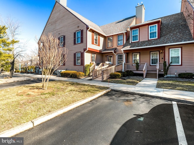 multi unit property featuring covered porch, a shingled roof, and a chimney