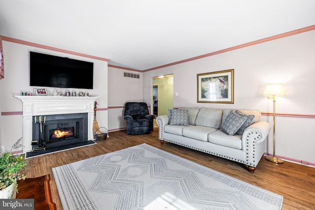 living room with visible vents, ornamental molding, wood finished floors, a warm lit fireplace, and baseboards