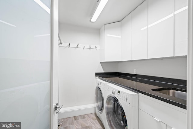 clothes washing area featuring cabinet space, washing machine and dryer, and a sink